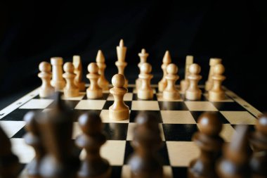 Gemideki beyaz ve siyah satranç taşlarını kapatın. Satranç tahtasındaki beyaz piyonun ilk hamlesine odaklan. Akıllı, mantıklı ve stratejik oyun kavramı