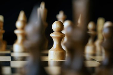 Gemideki beyaz ve siyah satranç taşlarını kapatın. Satranç tahtasındaki beyaz piyonun ilk hamlesine odaklan. Akıllı, mantıklı ve stratejik oyun kavramı