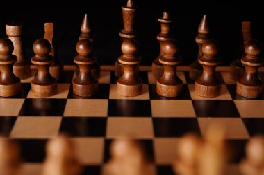 Gemideki siyah satranç taşlarını kapatın. Siyah arka planda satranç tahtasında iki sıra tahta figür. Akıllı, mantıklı ve stratejik oyun kavramı.