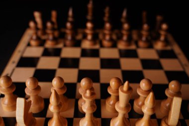 Satranç tahtasındaki beyaz ve siyah tahta parçaları. Siyah arkaplanda bir oyun sırasında kurulmuş bir satranç tahtası.