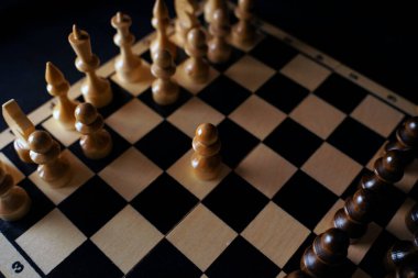 Gemideki siyah satranç taşlarını kapatın. Siyah arka planda satranç tahtasında iki sıra tahta figür. Akıllı, mantıklı ve stratejik oyun kavramı.