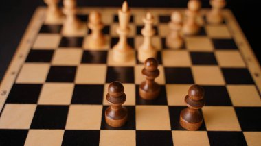 Gemide beyaz ve siyah tahta satranç taşlarını yakın çekim yapın. Siyah piyonlar, beyaz papaz ve vezirin satranç tahtasındaki piyonlarıyla karşılaşması. Akıllı, mantıklı ve stratejik oyun kavramı