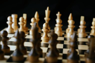 Gemideki beyaz ve siyah satranç taşlarını kapatın. Satranç tahtasındaki beyaz piyonun ilk hamlesine odaklan. Akıllı, mantıklı ve stratejik oyun kavramı