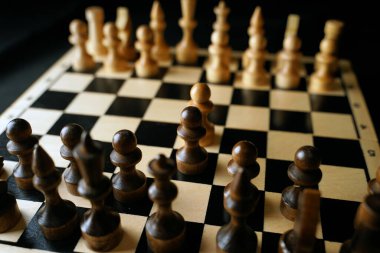 Gemideki siyah satranç taşlarını kapatın. Siyah arka planda satranç tahtasında iki sıra tahta figür. Akıllı, mantıklı ve stratejik oyun kavramı.