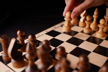 Gemide beyaz ve siyah tahta satranç taşlarını yakın çekim yapın. Kadının eli satranç tahtasındaki beyaz piyonu ilk hamlesini yapıyor. Akıllı, mantıklı ve stratejik oyun kavramı