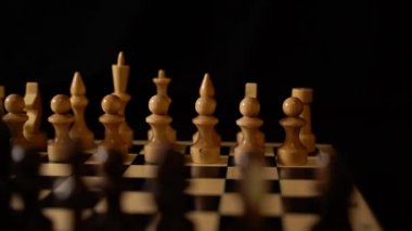 Satranç tahtasındaki beyaz ve siyah tahta parçaları. Siyah arkaplanda bir oyun sırasında kurulmuş bir satranç tahtası