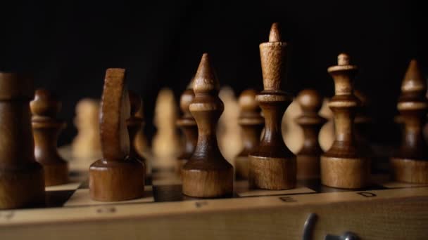 Primer plano de dos filas de piezas de ajedrez negro en el tablero de ajedrez. Mujeres mano derribando figuras de madera en el tablero de ajedrez sobre fondo negro. Movimiento lento. — Vídeos de Stock
