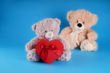 Kalp şeklinde kırmızı hediye kutusu olan sevimli oyuncak ayılara yakın durun. Mavi arka planda mevcut yumuşak peluş oyuncaklar. Tatil kavramı, hediyeler ve iyi ruh hali.