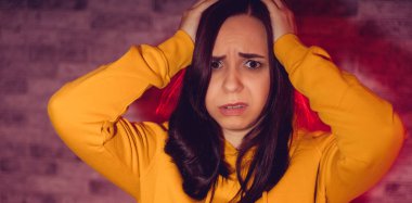 Elleriyle başını tutan mutsuz genç bir kadının portresi. Sarı kapüşonlu, baş ağrısından başını tutan üzgün kadını kapat.