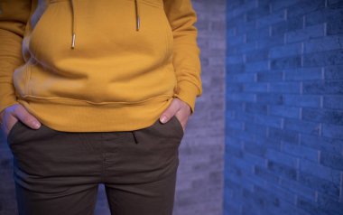 Genç bir kadının vücudunun ön tarafı tuğla bir duvara dayalı. Tanınmayan bir kadının yakınına ellerini pantolonunun cebine koy.