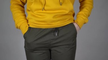 Tanınmayan bir kadına yakın çekim yap ve ellerini pantolonunun cebine sok. Gri arka planda boş ceplerini gösteren genç bir kadının vücudunun ön tarafı..