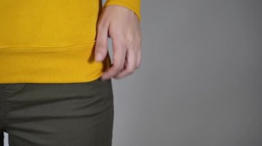 Gri arka planda genç bir kadının vücudunun ön yüzü. Tanınmayan bir kadına yaklaşın ve ellerini pantolonunun cebine sokun.