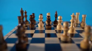 Satranç tahtasındaki beyaz ve siyah tahta parçaları. Mavi arkaplanda bir oyun sırasında kurulmuş bir satranç tahtası.