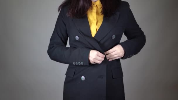 노란 블라우스와 검은 재킷을 입은 젊은 여성의 몸 일부가 앞에서 보인다. 얼굴도 알아볼 수없는 여자가 회색 배경 옷을 입고 양복 단추를 눌러. — 비디오