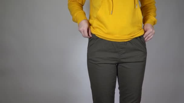 一个无法辨认的女人把她的手伸进她的裤子口袋 年轻女性身躯的正面视图 在灰色背景下展示空空的口袋 — 图库视频影像