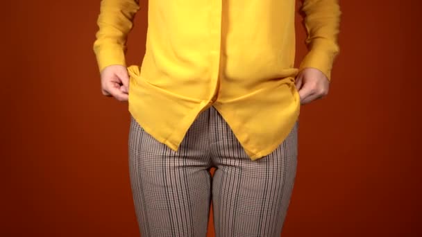 Zblízka nepoznatelná žena si strčila ruce do kapes kalhot. Pohled zepředu na část těla mladé ženy ukazující její prázdné kapsy na oranžovém pozadí. — Stock video