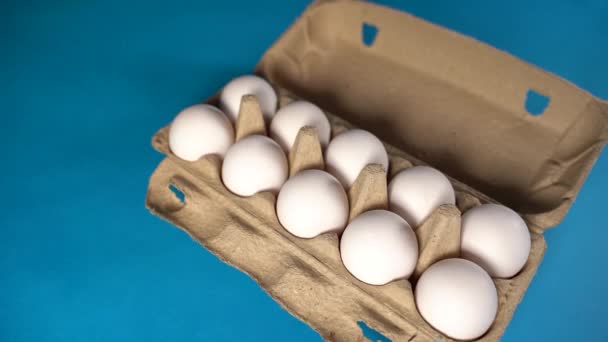 농장에서 날 것이고, 신선 한 흰 달걀 알을 푸른 배경에 있는 계란 상자에 넣었습니다. 카톤에 달걀이 들어 있어. 바구니에 들어 있는 달걀. 컨셉: 아침 식사를 위한 신선 한 달걀. — 비디오