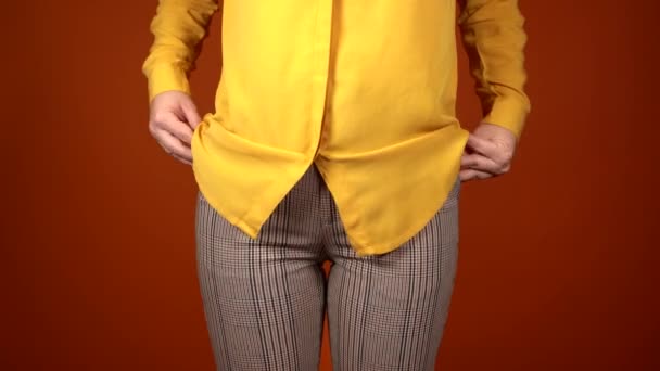 Vue de face sur la partie du corps de la jeune femelle en chemisier jaune et pantalon sur fond orange. Gros plan de femme méconnaissable mettre ses mains dans ses poches de pantalon. — Video