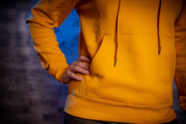 Sweatshirt 'lü genç bir kadının vücudunun ön yüzü. Gri tuğlalı arka planda elini destekleyen tanınmayan bir kadın figürü.