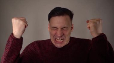 Turuncu arka planda kızgın bir adamın portresi. Saldırgan adam kameraya bakarak bağırıyor.