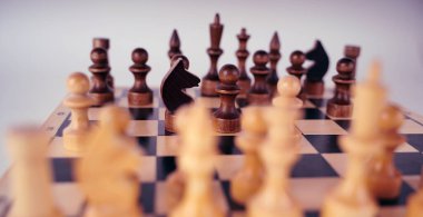 Satranç tahtasındaki beyaz ve siyah tahta parçaları. Gri arkaplandaki bir oyun sırasında kurulmuş bir satranç tahtası