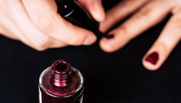 A woman dips nail brush in a jar color red gel nail polish, close-up