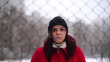 Şapkalı ve kırmızı ceketli genç bir kadın çitin arkasında dikiliyor. Dişi, kış mevsiminde çit çukurundan atlıyor. Yavaş çekim.