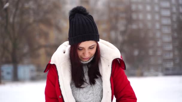 帽子の若い女性のクローズアップは 通りに立って 赤いジャケットに置きます 大人のブルネットは冬の季節に歩いて涼しい天気で暖まる — ストック動画