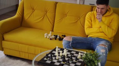 Sarı koltukta oturan ve odada satranç oynayan genç bir adam. Mantıksal bir masa oyunu oynayan bir erkek..