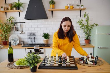 Mutfak masasında satranç oynayan genç bir kadın. Kadın mantıksal bir masa oyununda kendisiyle birlikte mutfakta oynuyor.