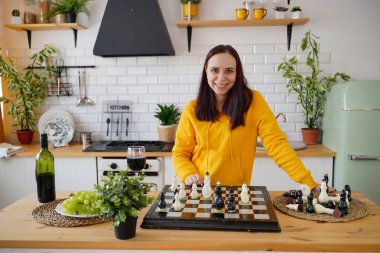 Mutfak masasında satranç oynayan genç bir kadın. Kadın mantıksal bir masa oyununda kendisiyle birlikte mutfakta oynuyor.