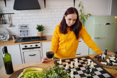 Mutfak masasında satranç oynayan genç bir kadın. Kadın mantıksal bir masa oyununda kendisiyle birlikte mutfakta oynuyor.