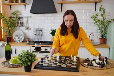 Mutfak masasında satranç oynayan genç bir kadın. Kadın mantıksal bir masa oyununda kendisiyle birlikte mutfakta oynuyor.