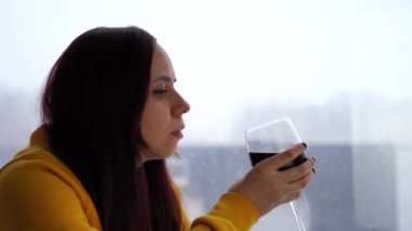 Rahatlamış genç bir kadın pencere kenarında oturup kırmızı şarap içiyor. Alkollü yetişkin esmer, karlı havada pencereden dışarı bakar ve bir şeyler düşünür..