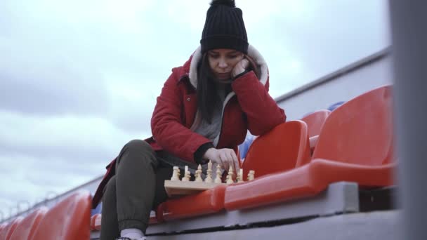 Jovem em roupas de inverno joga xadrez sentado nas