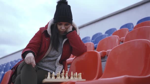 Kışlık Elbiseli Genç Kadın Satranç Oynuyor Stadyum Tribünlerinde Tek Başına — Stok video