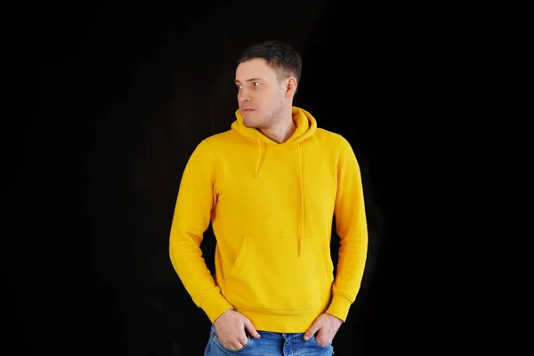 Portrait of young man on black background. Handsome guy in yellow hoodie posing on dark background