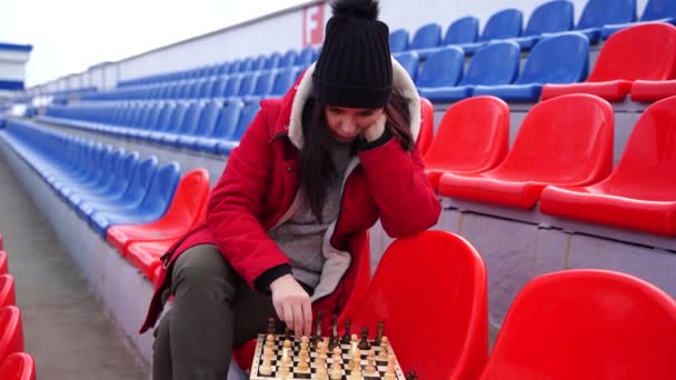 Egy Fiatal Téli Ruhában Sakkozik Egyedül Stadion Lelátóján Fekete Sapkában — Stock videók