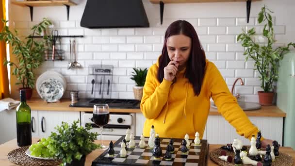 台所のテーブルでチェスをしている若い女性 女性は台所で自分自身と論理ボードゲームで遊ぶ — ストック動画