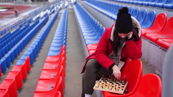Young Woman Winter Clothes Plays Chess Sitting Stadium Bleachers Alone — Stock Video
