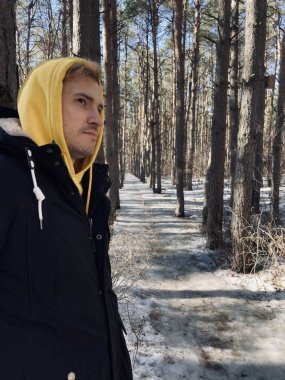 Ormanda yürüyen genç bir adamın portresi. Sarı kapüşonlu ve siyah ceketli yakışıklı, baharın başında ağaca yaslanmış.