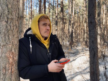 Ormanda yürürken cep telefonlu bir gencin portresi. Sarı kapüşonlu ve siyah ceketli yakışıklı bahar başında akıllı telefonlara bakıyor.