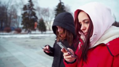 Şehir parkında akıllı telefonları karıştıran genç kadınlara yakın çekim. Cep telefonu kullanan kapüşonlu güzel kadınlar..