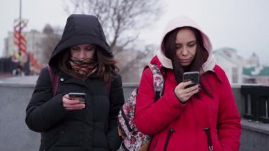 Şehir parkında akıllı telefonları karıştıran genç kadınlara yakın çekim. Cep telefonu kullanan kapüşonlu güzel kadınlar..
