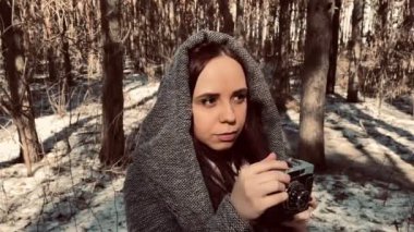 Gri ceketli genç bir kadın ormandaki eski fotoğraf makinesinde fotoğraf çekiyor. Güzel bir kadın eski bir kamerayla bahar başında fotoğraf çekiyor..
