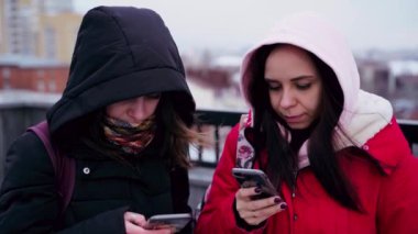 Şehir parkında akıllı telefonları karıştıran genç kadınlara yakın çekim. Cep telefonu kullanan kapüşonlu güzel kadınlar..