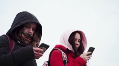 Şehir parkında akıllı telefonları karıştıran genç kadınlara yakın çekim. Cep telefonu kullanan kapüşonlu güzel kadınlar..