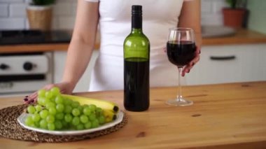 Tanımlanamayan bir kadın mutfakta kırmızı şarap içiyor. Meçhul kadın bardak ve içki alır..