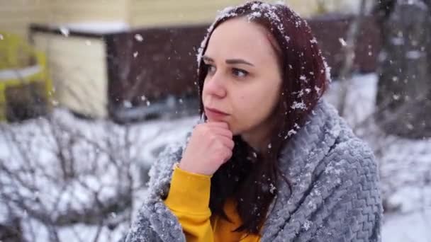一个年轻女子的近视把目光移开了 她坐在雪天的院子里的大街上 头脑清醒的女性裹着灰色格子花 — 图库视频影像