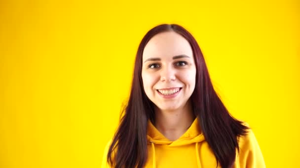 若い女性の笑顔と黄色の背景にカメラを見て閉じます。明るい背景でかなり女性の笑顔の肖像画. — ストック動画